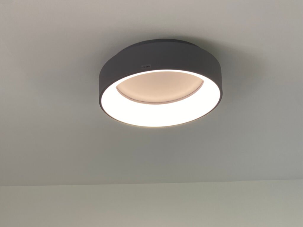 Modern LED ceiling light fixture mounted on a plain gray surface, emitting a bright glow.