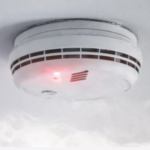 Close-up of a newly installed smoke and heat alarm on a ceiling, with a red activation light