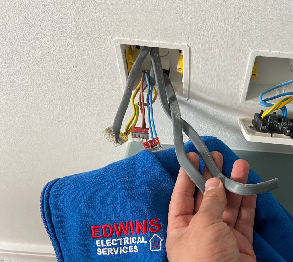 Close-up of an electrician's hands holding fresh new electrical cables in an open wall socket during a house rewiring