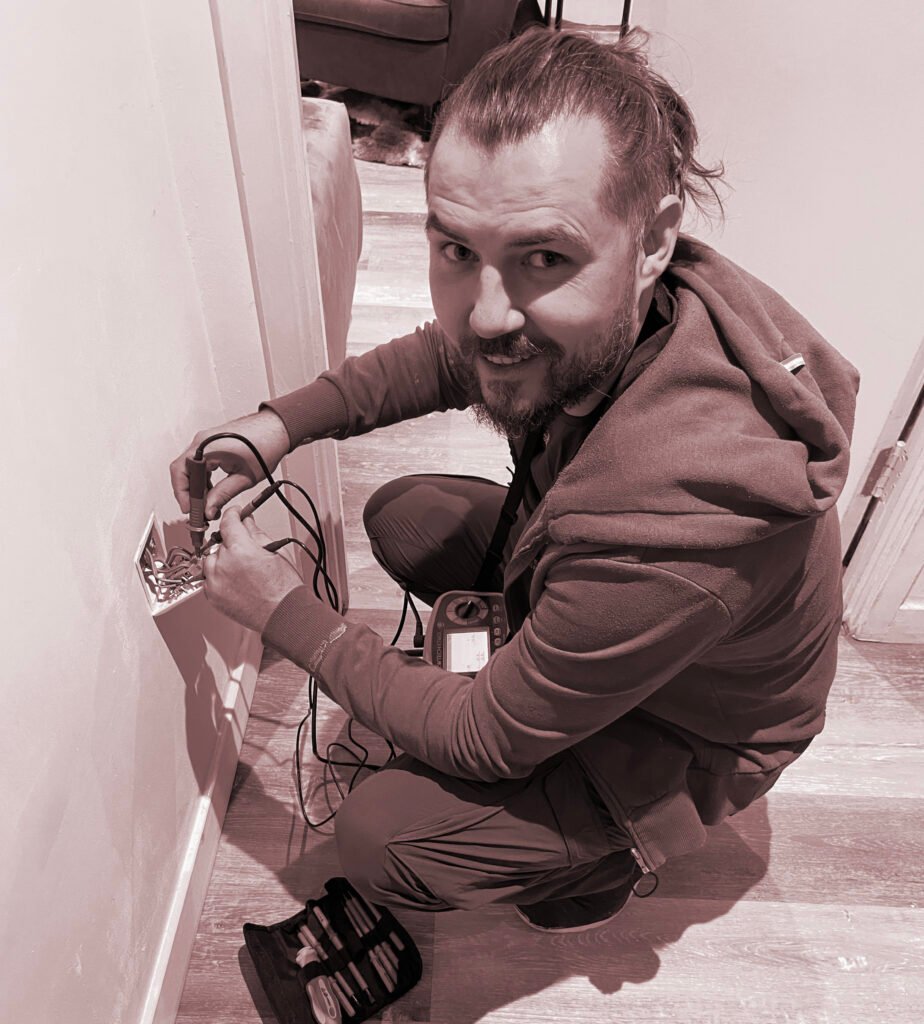 Electrician in East London fixing an electrical outlet, with tools and a multimeter.